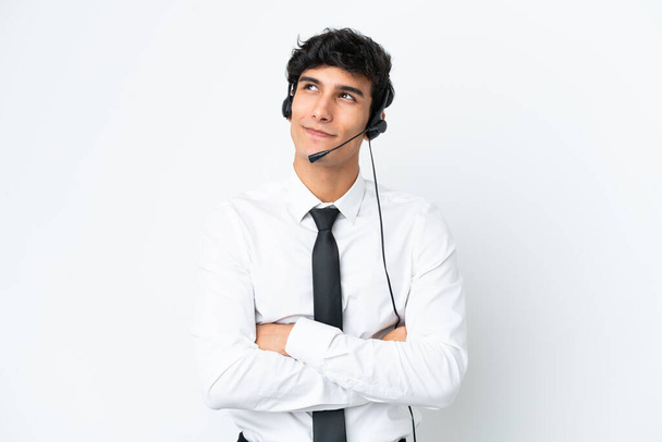 Hombre telemarketer trabajando con un auricular aislado sobre fondo blanco mirando hacia arriba mientras sonríe - Foto, imagen