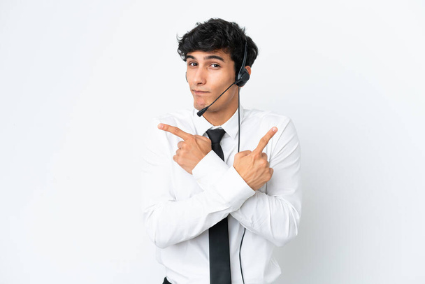 Hombre de telemarketer que trabaja con un auricular aislado sobre fondo blanco apuntando a los laterales que tienen dudas - Foto, imagen