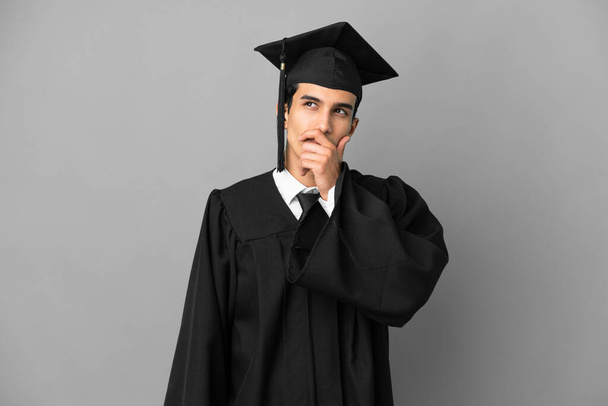 Νεαρός Αργεντινός απόφοιτος πανεπιστημίου απομονωμένος σε γκρίζο φόντο έχοντας αμφιβολίες και με έκφραση σύγχυσης - Φωτογραφία, εικόνα