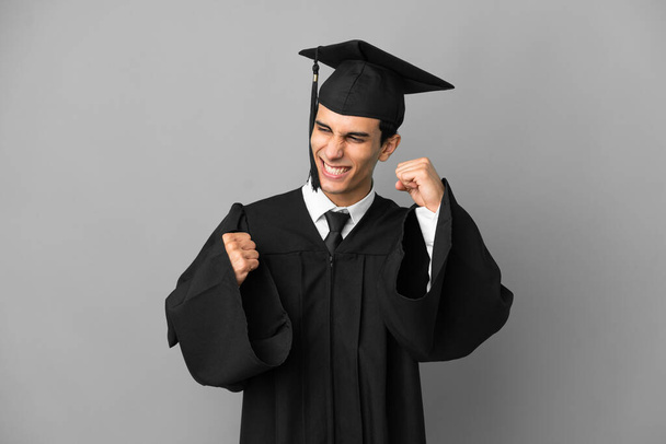 Young Argentinian university graduate isolated on grey background celebrating a victory - Foto, Imagen