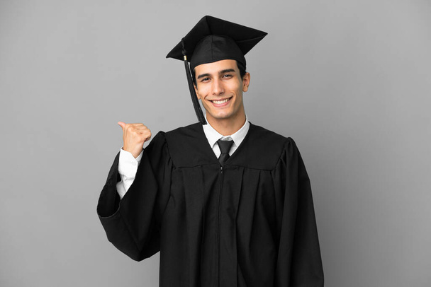 Mladý argentinský vysokoškolský absolvent izolovaný na šedém pozadí ukazující na stranu prezentovat produkt - Fotografie, Obrázek
