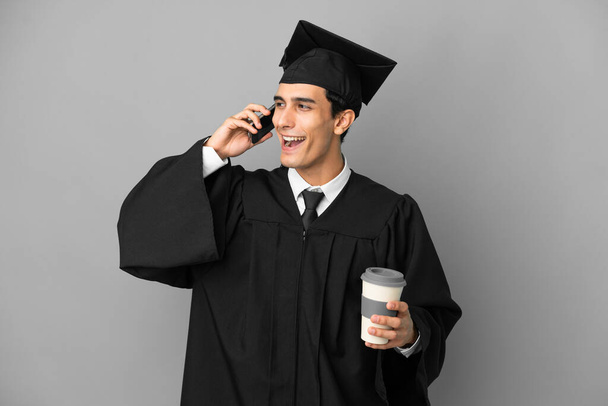 Young Argentinian university graduate isolated on grey background keeping a conversation with the mobile phone - Photo, Image