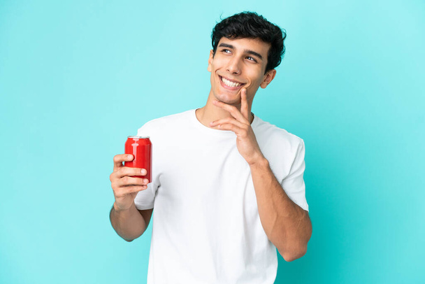 Young Argentinian man holding a refreshment isolated on blue background looking up while smiling - Foto, Bild