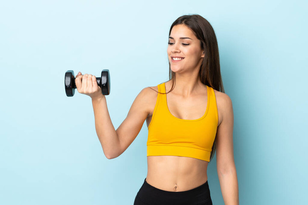 Young caucasian woman making weightlifting isolated on blue background with happy expression - 写真・画像