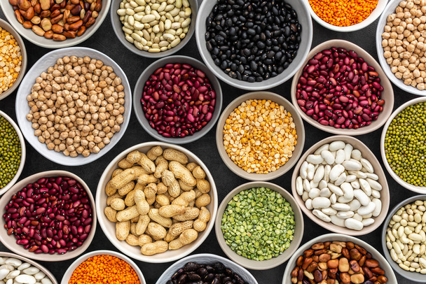 Different types of legumes in bowls, green with yellow peas and mung beans, chickpeas and peanuts, colored beans and lentils, top view - Photo, image