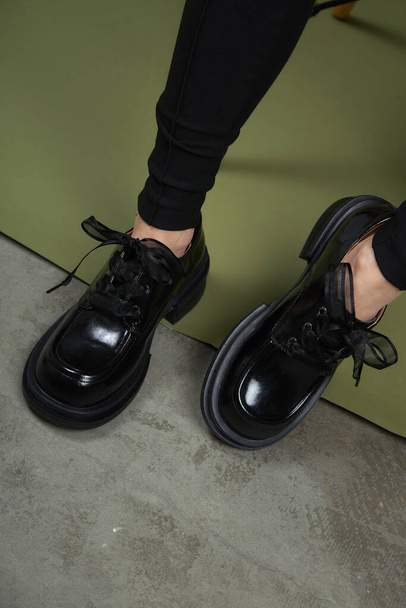 Vrouwelijke benen in zwarte laarzen op groene achtergrond. Casual lifestyle concept foto. Fashion schoenen gemaakt van eco-leer lente-zomer 2022. - Foto, afbeelding