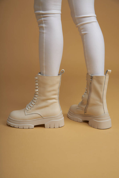 Fashionable woman with beige boots, leather shoes, studio shot. Casual lifestyle concept photo on a yellow pastel background. Fashion shoes made of eco-leather spring-summer 2022. - 写真・画像