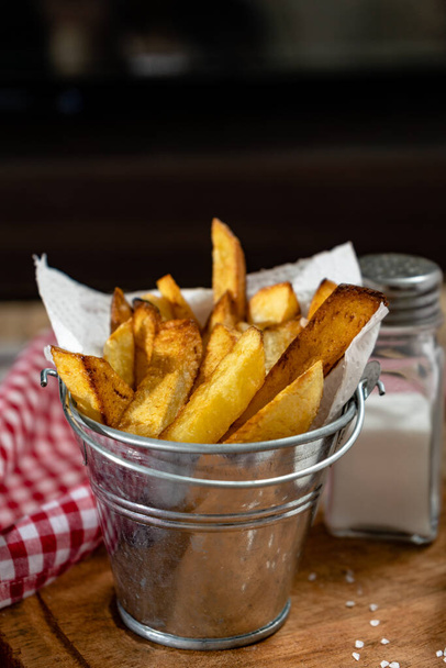 French fries in a metal pot with aioli and ketchup on a wooden board. Vertical orientation, copy-space. - Foto, Imagen