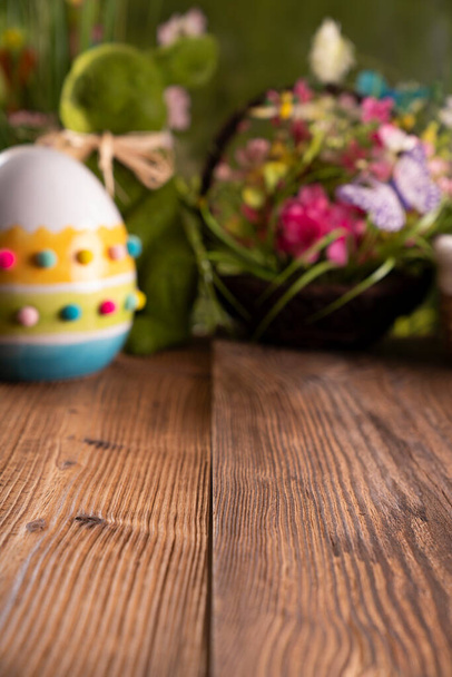 Пасха. Пасхальные украшения на деревенском деревянном столе. Пасхальный кролик, пасхальные яйца в корзине и листья капусты. Букеты весенних цветов.  - Фото, изображение