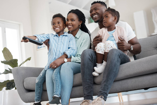 Was auch immer im Fernsehen läuft. Flachbild einer liebevollen jungen vierköpfigen Familie, die zu Hause im Wohnzimmer fernsieht. - Foto, Bild
