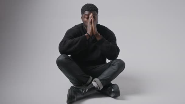 Bello afroamericano seduto sul pavimento mostrando disperazione muovendo le mani e la testa grigio sfondo copia spazio  - Filmati, video