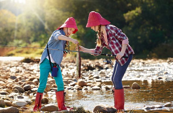 Fishing buddies having fun. Shot of two young girls fishing by a river. - Zdjęcie, obraz