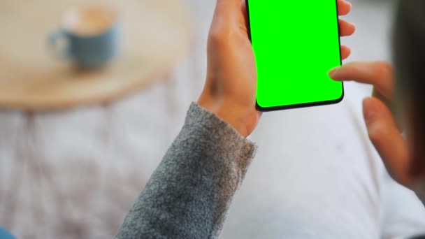 Kobieta w domu za pomocą smartfona z zielonym ekranem makiety w trybie pionowym. Dziewczyna przeglądająca Internet, oglądająca treści, filmy - Materiał filmowy, wideo