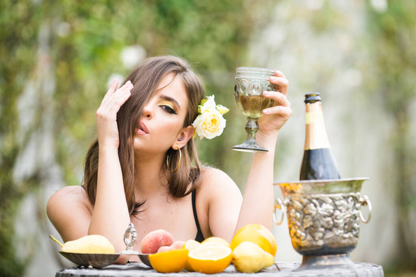 Sexy woman with fresh fruit on a table in park outdoors. Sensual young woman drink champagne. - Φωτογραφία, εικόνα