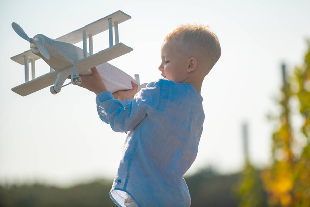 Child pilot with toy airplane dreams of traveling in summer in nature. Kids dreams. Child plays with a toy plane and dreams of becoming a pilot. Childhood dream imagination concept. - 写真・画像
