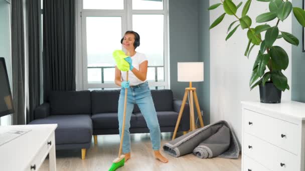 Femme en casque nettoyant la maison et s'amusant à danser avec un balai et un gant de toilette. Mouvement lent - Séquence, vidéo