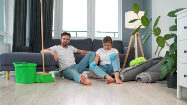 Tired couple sits on the floor in a room and high five each other after they finish cleaning the house. - Filmmaterial, Video