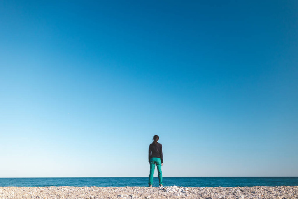 Ένα κορίτσι περπατά μόνο του στην παραλία, μια γυναίκα κοιτάζει τη θάλασσα, μια μελαχρινή στο φόντο της θάλασσας και των βουνών, αναπαύεται στις ακτές της θάλασσας - Φωτογραφία, εικόνα