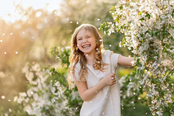 Πορτρέτο του κοριτσιού που γελάει κάτω από πεσμένα πέταλα λουλουδιών κερασιάς την άνοιξη. - Φωτογραφία, εικόνα
