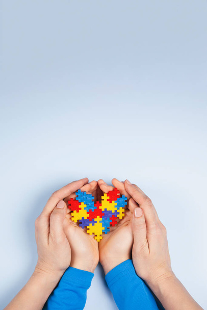 World autism awareness day concept. Mani per adulti e bambini che tengono il cuore puzzle su sfondo azzurro. Vista dall'alto - Foto, immagini