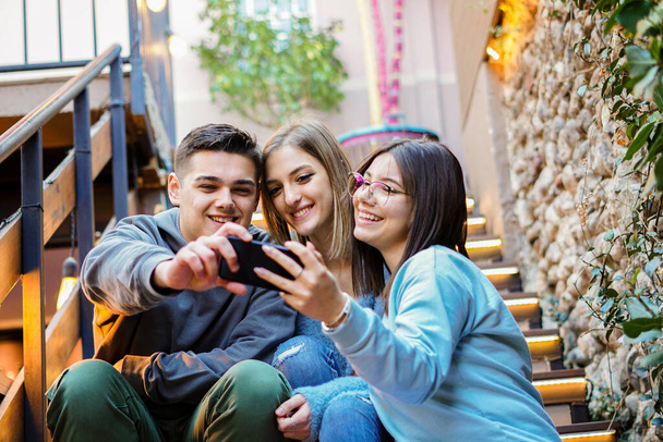 Młodzi ludzie korzystający razem ze smartfona - studenci bawią się telefonem komórkowym - Zdjęcie, obraz