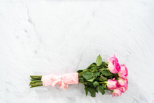 ピンク色のバラの花束は、具体的な背景にピンクのリボンとピンクの包装紙に包まれました。. - 写真・画像
