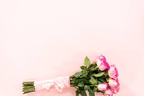 Bouquet of pink roses wrapped in pink wrapping paper with a pink ribbon on a pink background. - Foto, Imagem