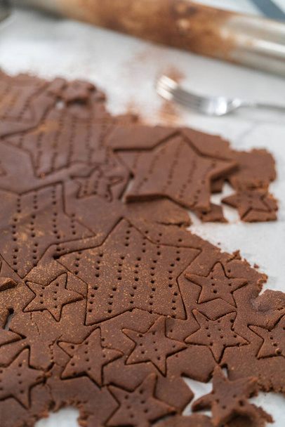 Cięcie czekoladowych krakersów w kształcie gwiazdy z ciasta nożem do ciastek. - Zdjęcie, obraz