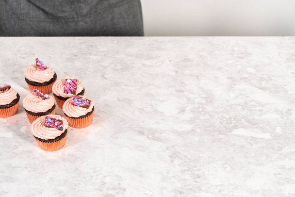 Упаковка свіжоспечені шоколадні полуничні кекси, прикрашені гастрономічними міні-рожевими шоколадними цукерками в білий паперовий кекс
. - Фото, зображення