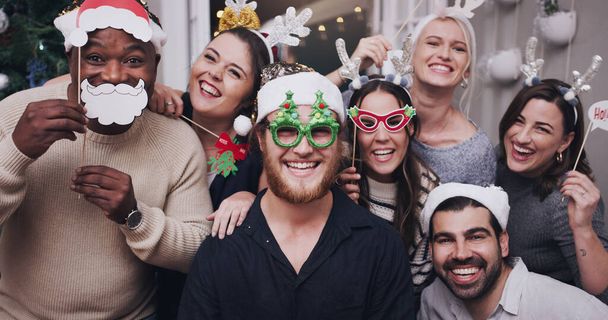 Φορέστε τα καπέλα σας, τα Χριστούγεννα είναι εδώ. Προσωπογραφία μιας ομάδας νεαρών φίλων που φορούν αστεία καπέλα και γυαλιά σε Χριστουγεννιάτικο πάρτι. - Φωτογραφία, εικόνα