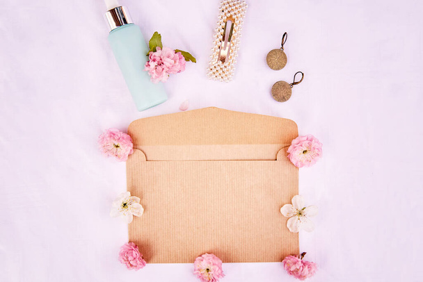 Elegante mockup sobre de primavera femenina con flores rosadas, accesorios, regalo cosmético sobre fondo blanco de tela. 8 de marzo concepto. Foto de alta calidad - Foto, imagen