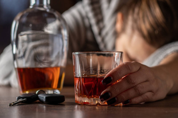 Betrunkene Frau, die in der Nähe von Whiskeygläsern schläft, starke Alkoholikerin, die nach Alkohol schlafend ohnmächtig wird, Alkoholismus-Problem, Alkoholabhängigkeitskonzept. Autoschlüssel auf Tisch liegend. - Foto, Bild