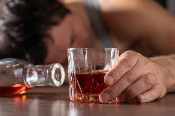 Alcoholismo, adicción al alcohol y concepto de personas - alcohólico masculino con vaso de whisky acostado o durmiendo en la mesa. - Foto, Imagen