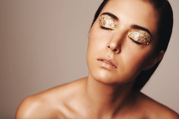 Beauty shines through. Studio shot of a beautiful woman with eyes closed and gold eye makeup. - Photo, Image
