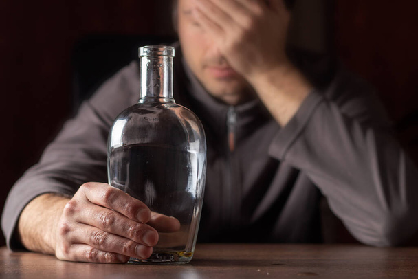 Homem bêbado segurando a cabeça com uma garrafa quase vazia de álcool. - Foto, Imagem