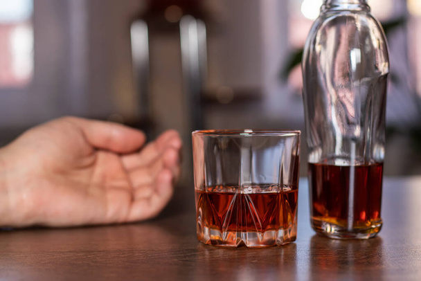 Alkoholismus, skleněná whisky a lidská ruka leží na stole. Léčba závislosti na alkoholu, trpí zneužíváním alkoholismu. - Fotografie, Obrázek