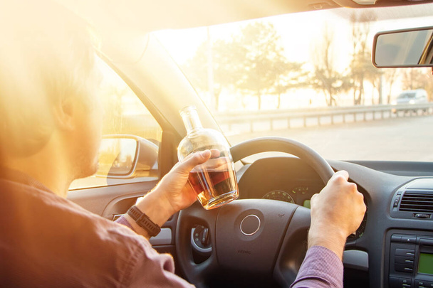 Mężczyzna pijący alkohol podczas jazdy samochodem o zachodzie słońca. - Zdjęcie, obraz