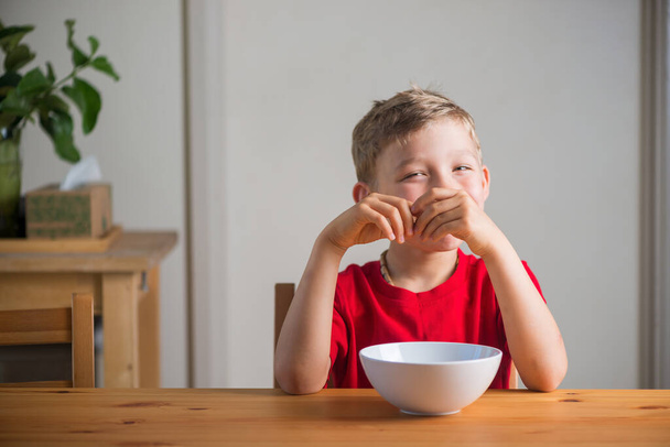 Uśmiechnięty chłopiec je granolę na śniadanie. Prawdziwe wyrażenia. - Zdjęcie, obraz