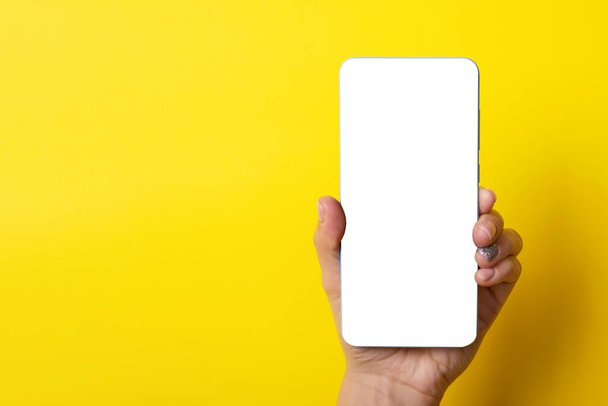 Smartphone en mano femenina sobre fondo amarillo, imagen de diseño - Foto, imagen