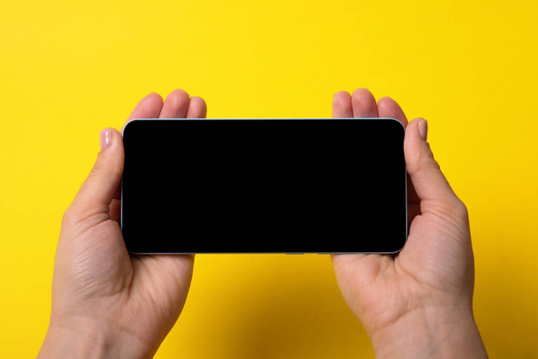 Smartphone en manos femeninas con pantalla negra sobre fondo amarillo - Foto, imagen