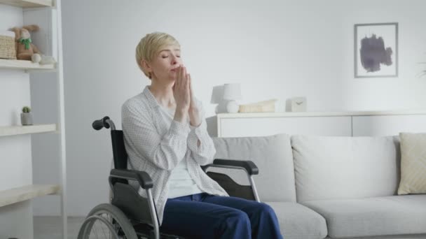 Madura mujer desesperada con lesión en la columna vertebral rezando a Gao, sentado en silla de ruedas en el interior de casa, espacio vacío - Imágenes, Vídeo
