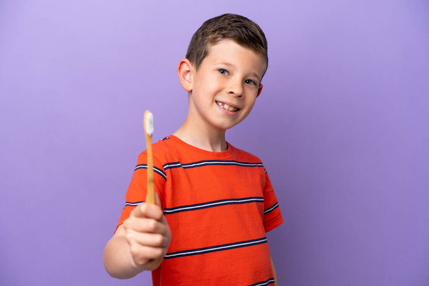 Μικρό αγόρι βούρτσισμα των δοντιών απομονώνονται σε μωβ φόντο με ευτυχισμένη έκφραση - Φωτογραφία, εικόνα