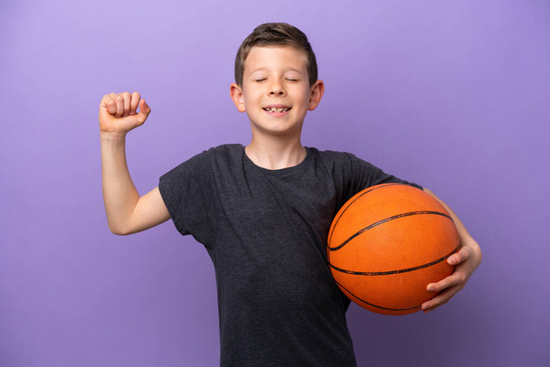 紫色の背景に孤立したバスケットボールをしている小さな男の子は強いジェスチャーをします - 写真・画像