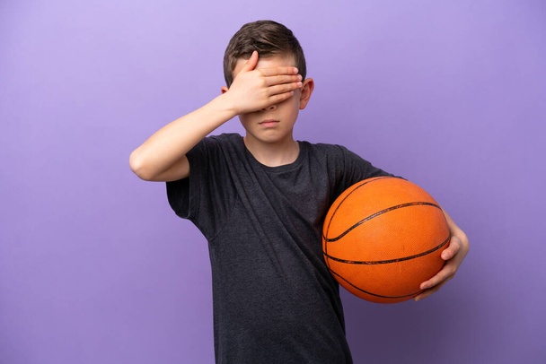 Mały chłopiec grający w koszykówkę, odizolowany na fioletowym tle, zakrywający oczy dłońmi. Nie chcę nic widzieć. - Zdjęcie, obraz