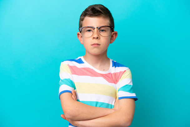 Kleiner Junge isoliert auf blauem Hintergrund mit Brille und verschränkten Armen - Foto, Bild