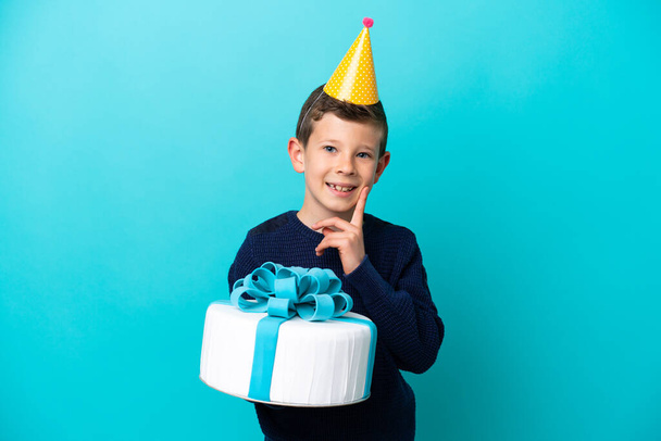 Kisfiú kezében születésnapi torta elszigetelt kék háttér gondolkodás egy ötlet, miközben felnéz - Fotó, kép