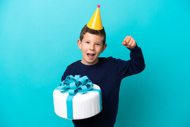 Маленький мальчик держит торт на голубом фоне, празднуя победу - Фото, изображение