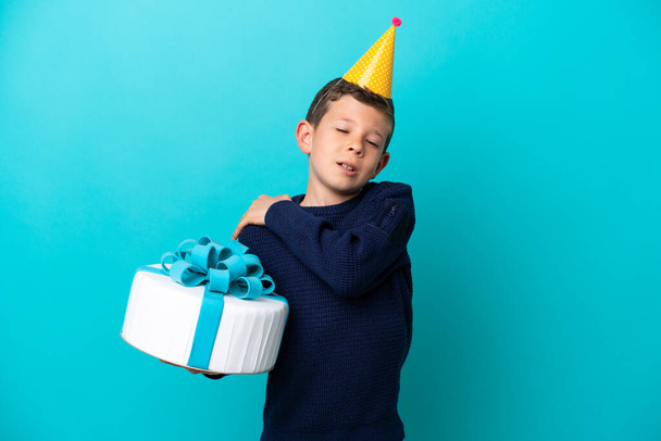 Маленький мальчик держит торт на день рождения изолирован на синем фоне страдает от боли в плече за то, что сделал усилие - Фото, изображение