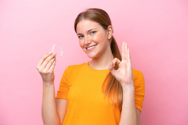 Young caucasian woman holding invisaging isolated on pink background showing ok sign with fingers - Photo, image