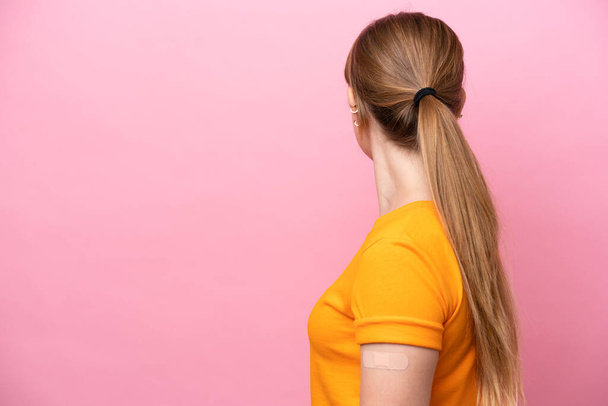 Young caucasian woman wearing band aid isolated on pink background in back position - Foto, Imagen